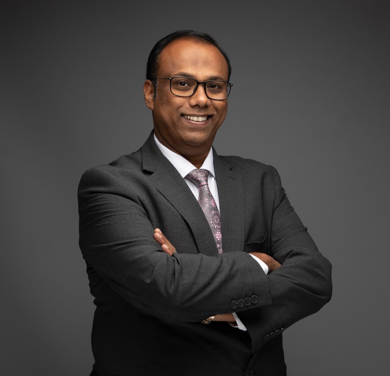 Renoy smiling in a dark suit with his arms crossed
